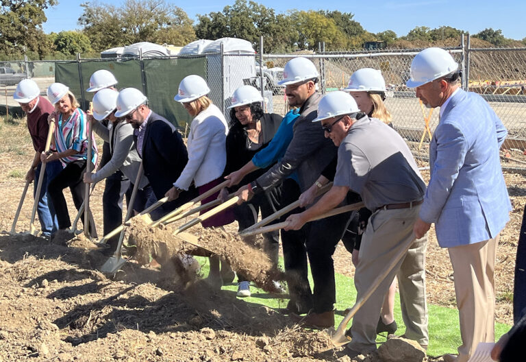 Eight people wearing hard hats digging with shovels