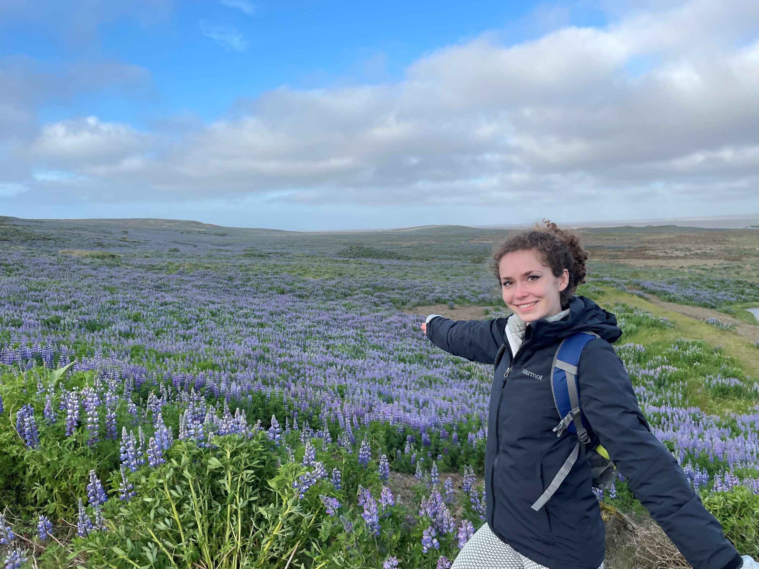 Woman in a jacket standing in front of a blue sky and a field of purple flowers